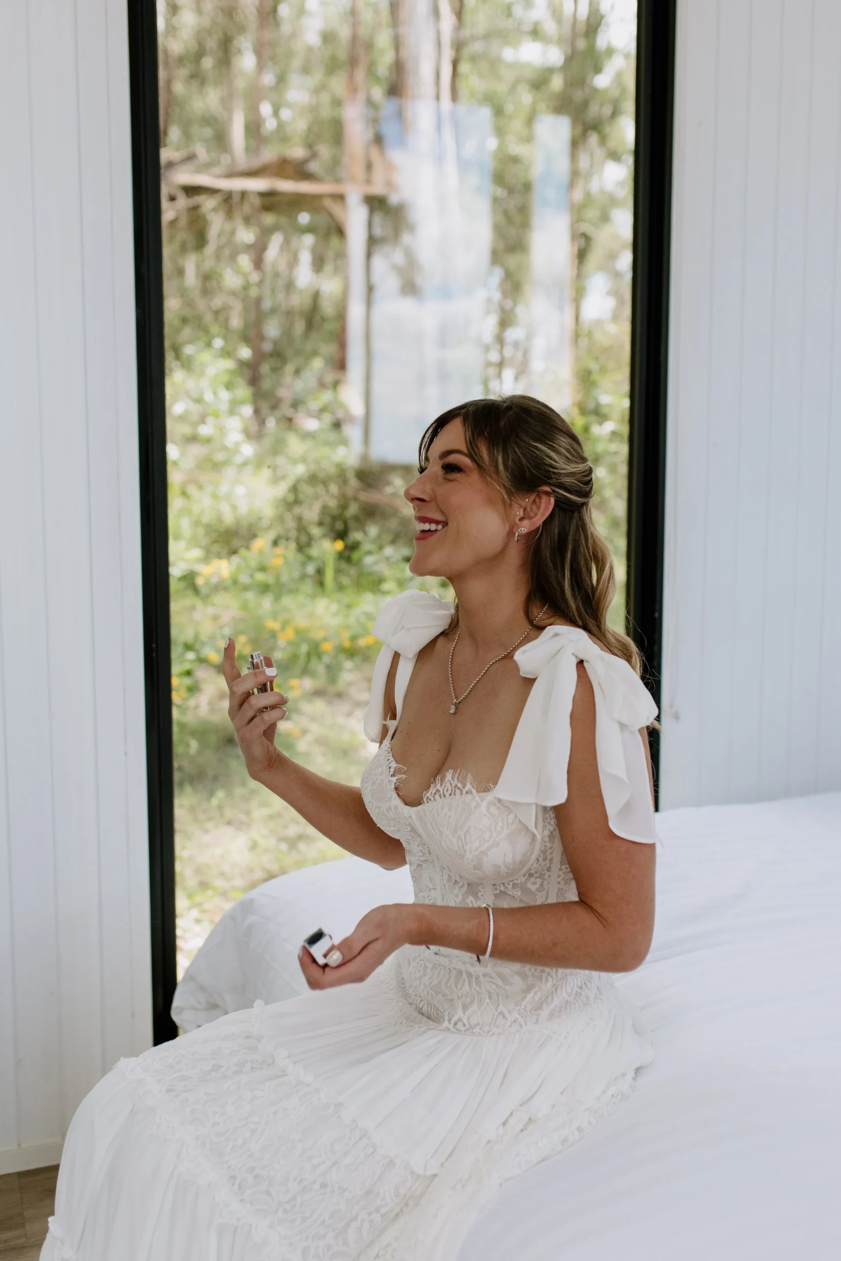 bride sprays perfume while sitting on a bed