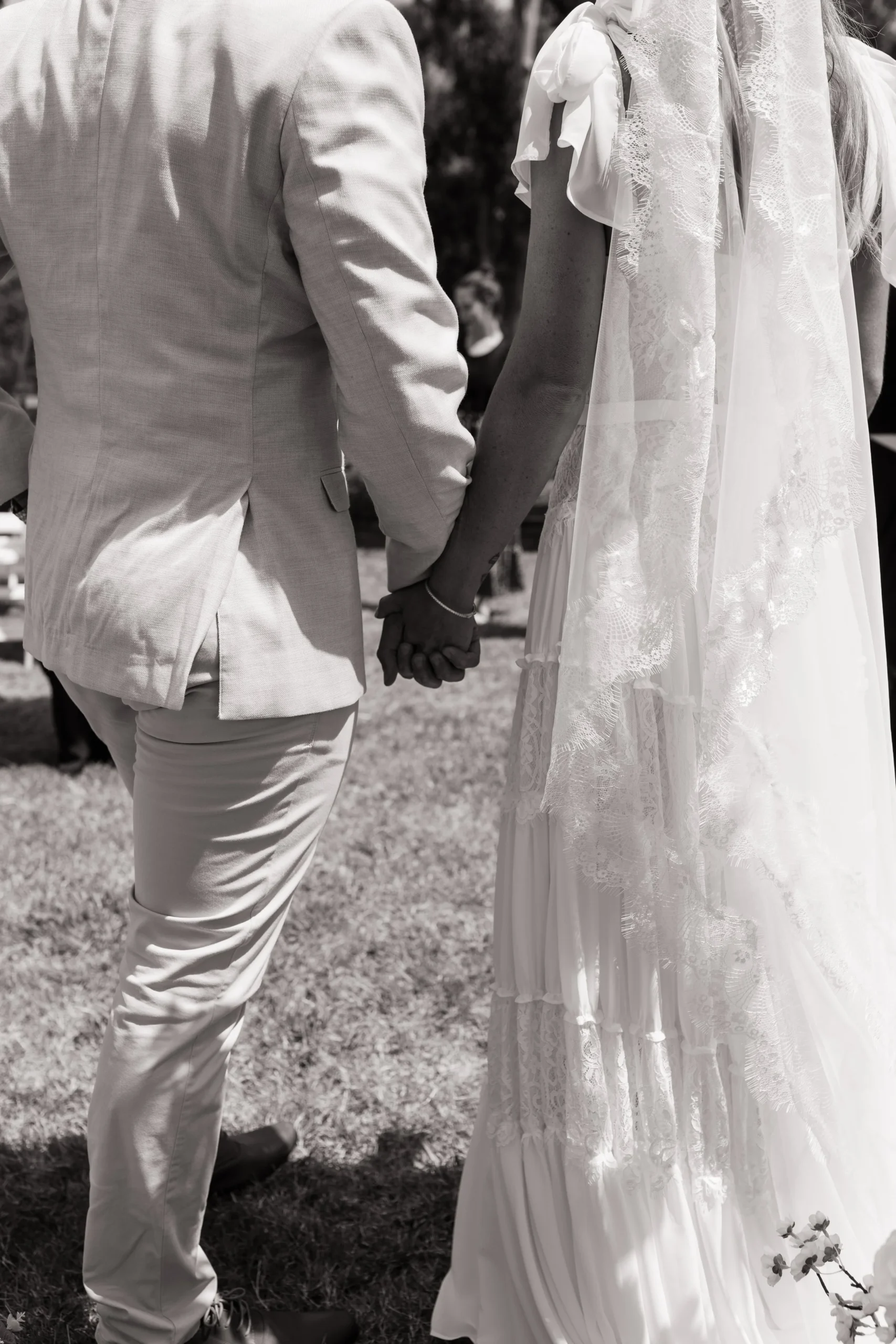 black and white image of a bride and groom holding hands facing away from the camera