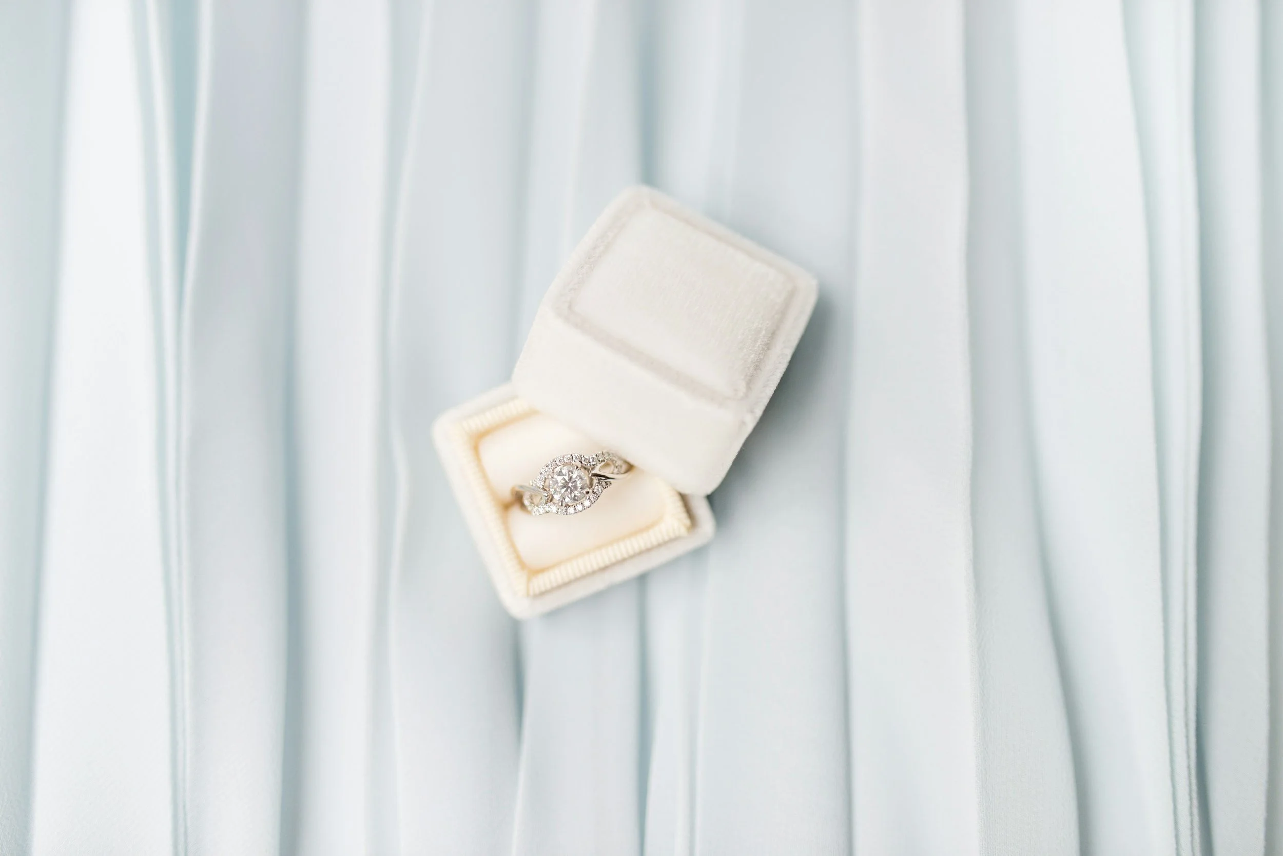 white ring box with engagement ring on a blue fabric background