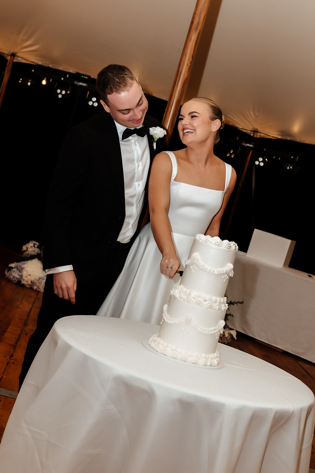 Newlyweds smile at each other as they cut their 2 tier wedding cake