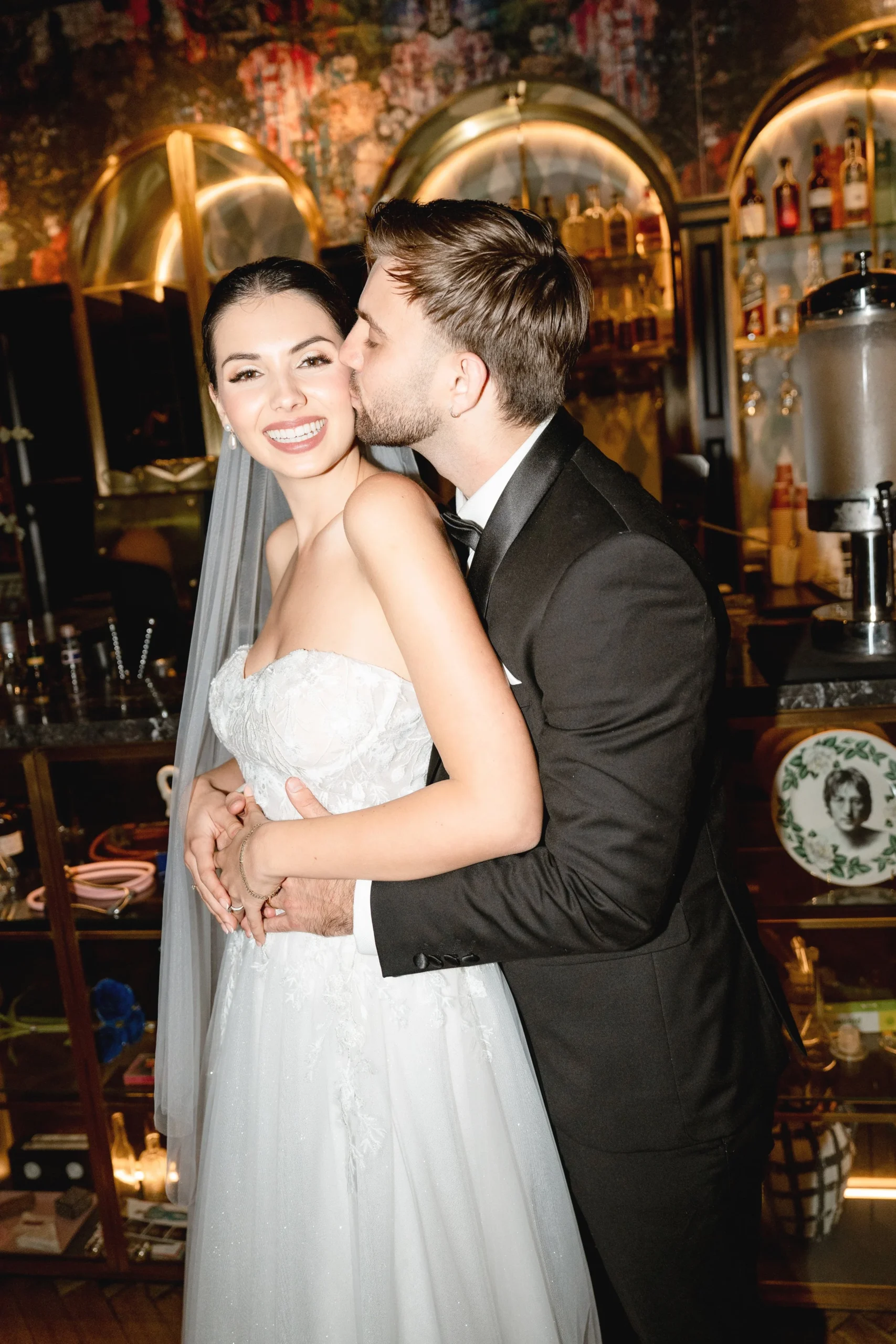 Groom kissing wife on cheek in front of a trendy bar